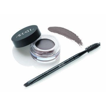 Uncapped container of Ardell Brow Pomade alongside brush/spoolie tool with pomade swatched onto background to show color